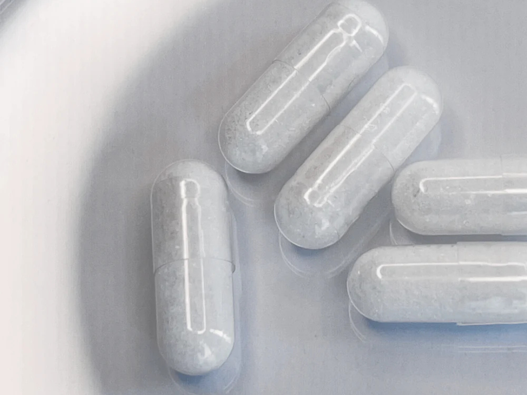 Close-up of NR (nicotinamide riboside) capsules – clear HPMC shells with white powder on a blister tray